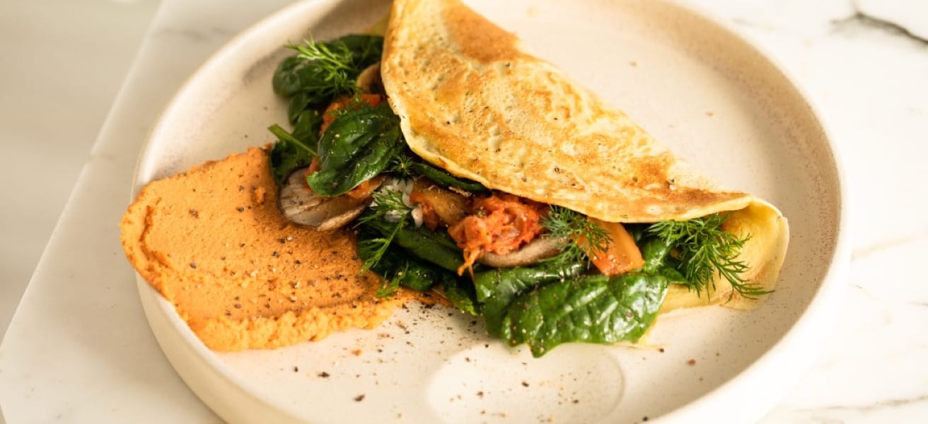 An Omelette filled with vegetables and meat on. white plate.